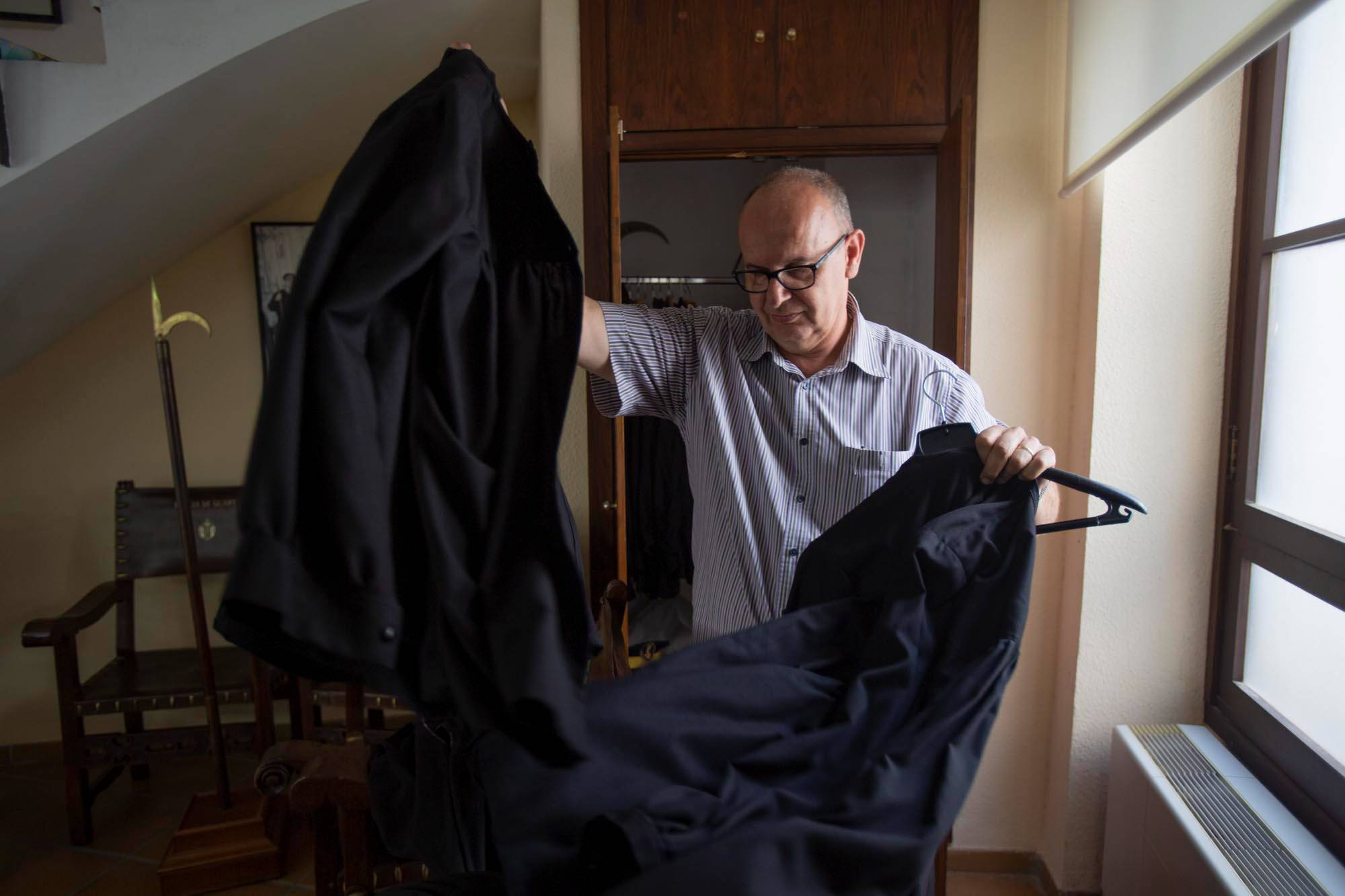 Color photograph of a man near a window lifting up a black judicial robe.